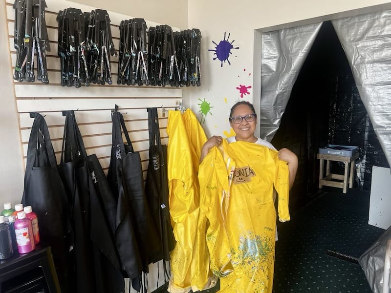 Sonia Robinson holds a paint poncho next to the splatter room inside her art studio, Color Me Happy, in Sterling, Illinois.