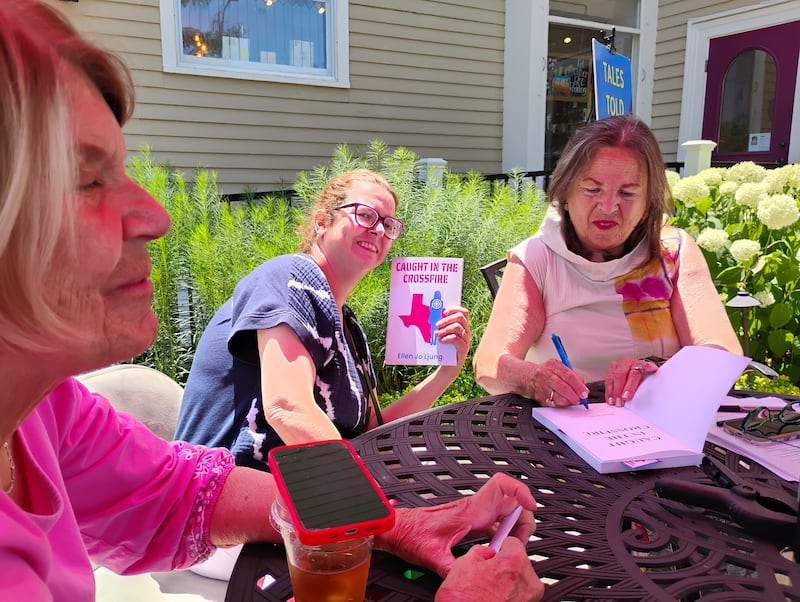 Geneva author Ellen Jo Ljung, (right) signs a copy of her first novel, 'Caught in the Crossfire,' for Vadie Schultz, (far left) on Saturday, June 28, at Harvey's Tales in Geneva. She also signed a book for Cristine Clemente Dos Santos (center) also of Geneva. Ljung's book is about a progressive teacher who lands in the middle of Texas politics in the 2022-23 school year.