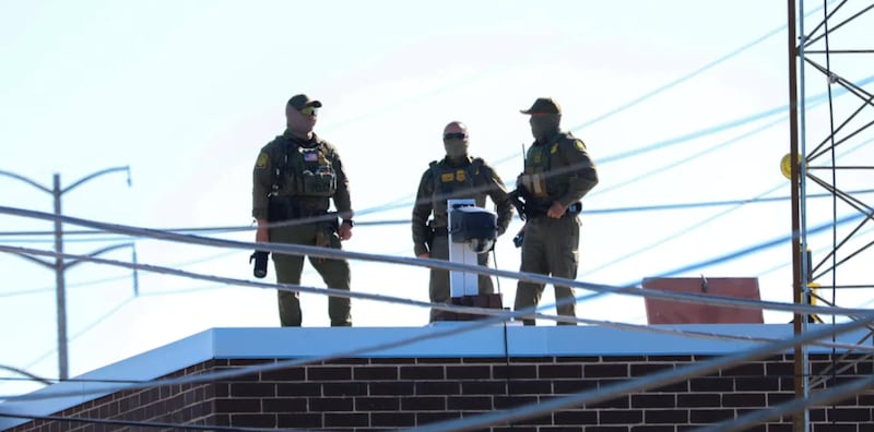 Three men in Customs and Border Protection uniforms stand on the roof of a Broadview immigration facility taking pictures of the surrounding area on Oct. 9, 2025.