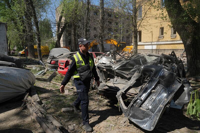 A police officer passes by remains of the cars damaged in the Russian missile attack that hit residential houses Thursday killing 12 civilians and injuring 87 in Kyiv, Ukraine, Friday, April 25, 2025. (AP Photo/Efrem Lukatsky)