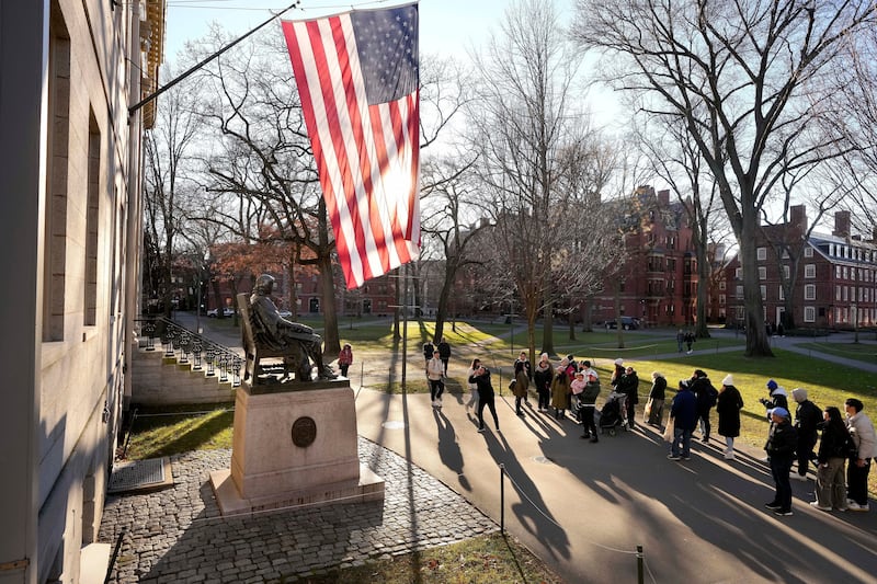 FILE - People take photos near a John Harvard statue, left, on the Harvard University campus.