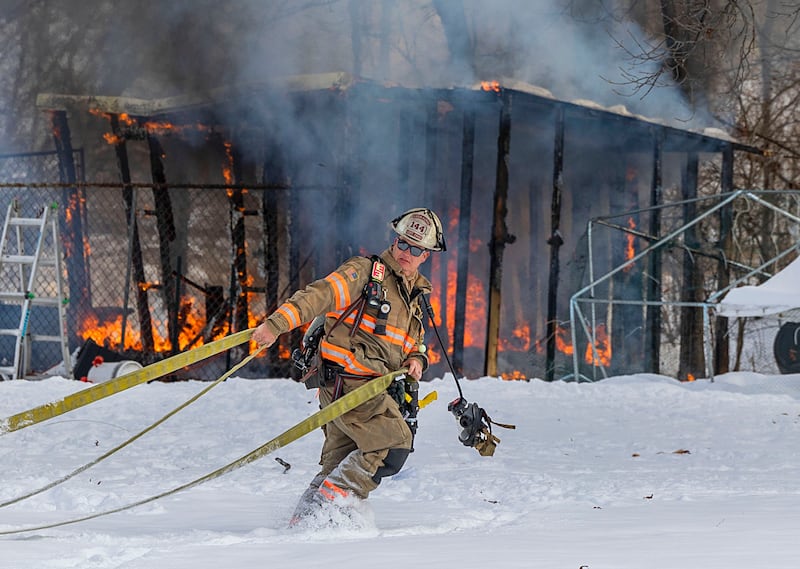 A firefighter drags a hose through the deep snow Monday, Dec. 8, 2025, to douse a shed fire at 1558 Joliet Way in Dixon.
