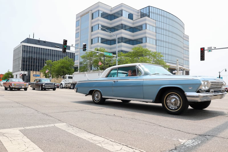 A passenger waves from a classic car as it travels in a group along Court Street in Kankakee as part of the Hot Rod Power Tour 2025 on Tuesday, June 10, 2025. Over 5,000 cars passed through the city's main artery en route to Joliet as part of the five-day traveling car show.