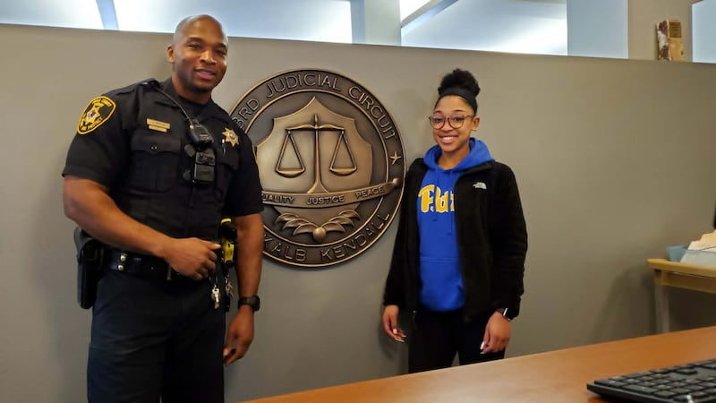DeKalb County Sheriff's deputy Antonio Watson (left) and his daughter Sariyah Watson, of DeKalb, smile in front of the sheriff's office crest in this undated photo. Sariyah was killed at 21 on Sunday, May 10, 2026, in a wrong-way crash on Interstate 88 near Aurora.