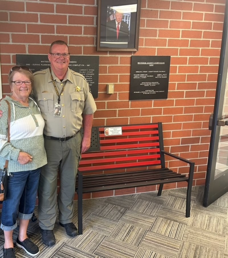 Linda Millerschone and Whiteside County Sheriff John Booker pose near the bench placed at the Whiteside County Sheriff's Office in memory of Deputy Gordie Millerschone.