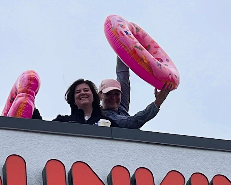 Members of the Joliet Police Department's record section wave giant inflatable donuts on Friday, May 15, 2026, for the 23rd annual Dunkin' Cop on a Rooftop event in Joliet.