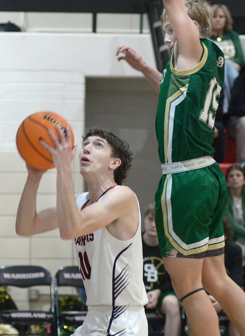 Woodland’s Jaron Follmer eyes the basket for shot as St Bede’s Geno Dinges jumps to block in the 1st quarter Friday at Woodland.