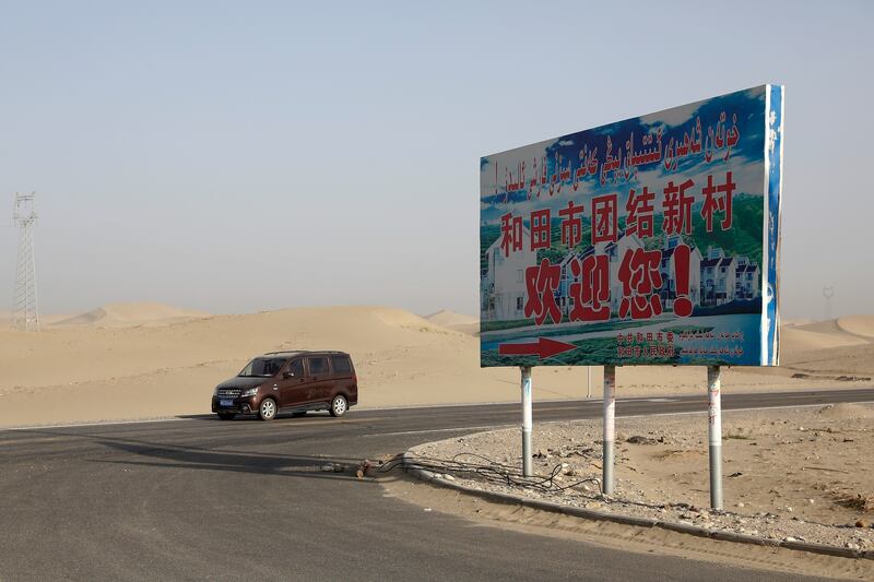 FILE - A car drives through a desert where a signboard which reads "Welcome to the Hotan Unity New Village" is seen on display in Hotan, in western China's Xinjiang region on Sept. 21, 2018. (AP Photo/Andy Wong, File)