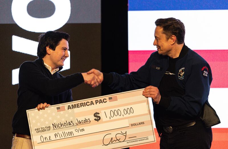 FILE - Elon Musk hands over a million dollar check to Nicholas Jacobs during a town hall in Green Bay, Wis., March 30, 2025. (AP Photo/Jeffrey Phelps, File)