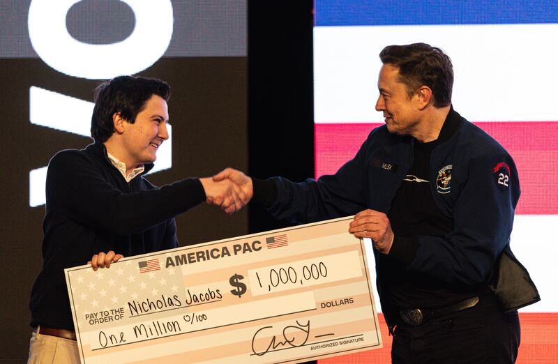FILE - Elon Musk hands over a million dollar check to Nicholas Jacobs during a town hall in Green Bay, Wis., March 30, 2025. (AP Photo/Jeffrey Phelps, File)