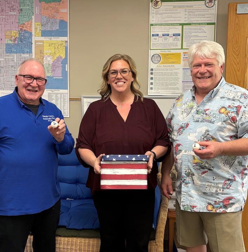 Carmen Polvere, a DeKalb County Board Democratic party candidate, and Brian Siwicki, the chair of the DeKalb County Republican central committee, hold ping pong balls next to DeKalb County Clerk and Recorder Tasha Sims on May 7, 2025, for a lottery to determine which party appears first on the ballot for the next general election.