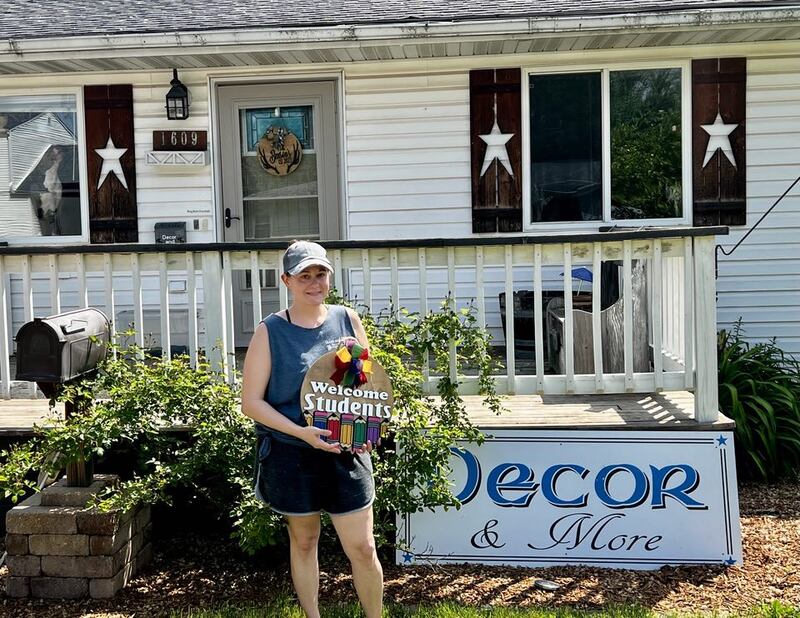 Lynn Benson holds a wooden sign in front of her home-based business, Decor & More, in Rock Falls, Illinois.