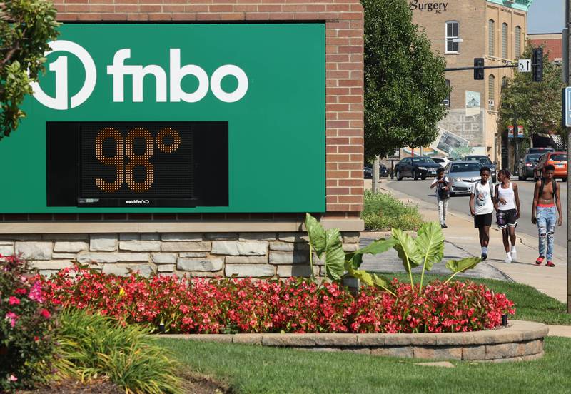 Pedestrians and vehicles travel down Lincoln Highway in DeKalb Wednesday, Aug. 23, 2023, in front of the sign at the First National Bank of Omaha which reads 98 degrees. Temperatures climbed into the high 90’s Wednesday with more hot weather expected Thursday.