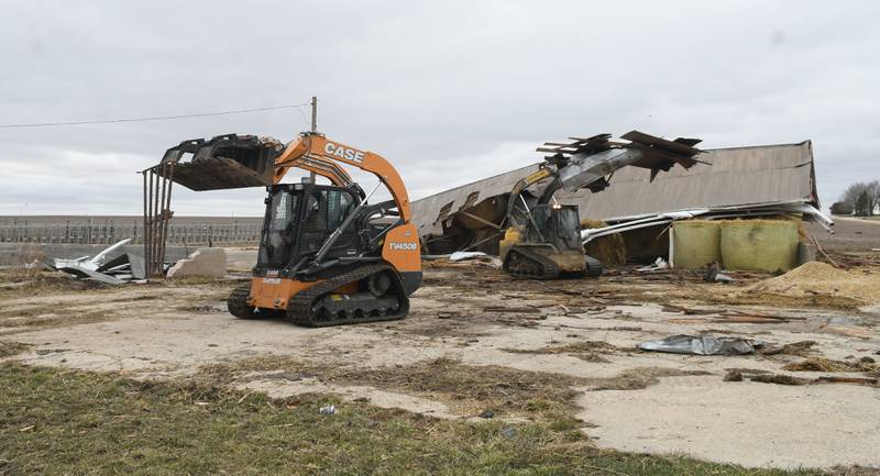 Rob Gunderson uses a skid steer to move a iron gate from one of the damaged storm sheds as a friend holds the shed's roof on Saturday. Friday night's storm ripped through his dairy farm west between Shannon and Forreston. No livestock were injured.