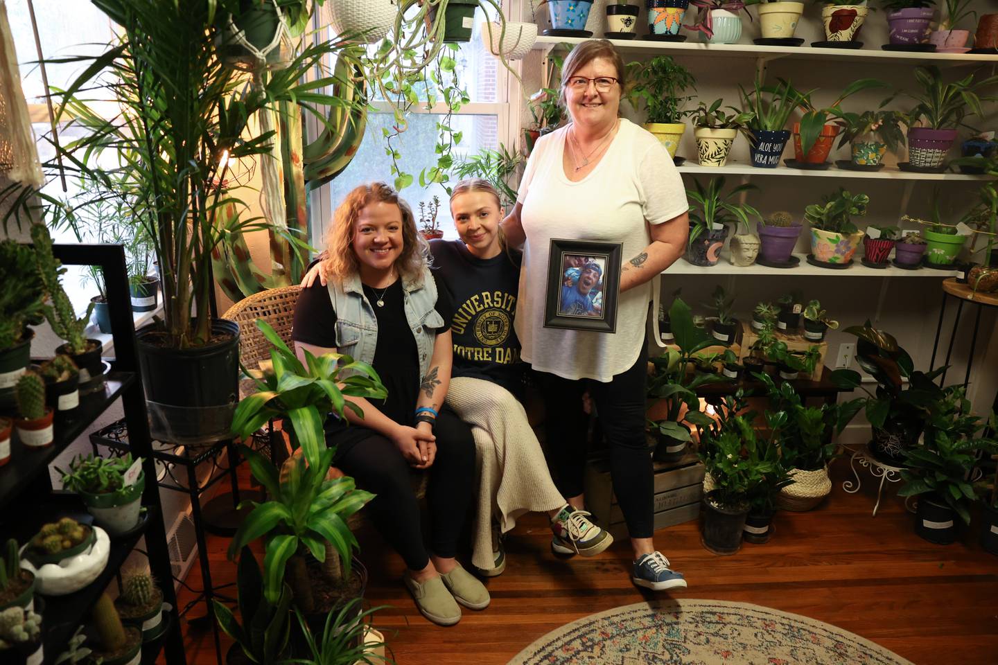 Marianne Searing holds a photo of her son, Nate, standing with her daughters, Ashley, left, and Hailey at their shop RejuveNate in Crest Hill on Friday, May 12, 2023.