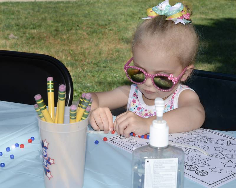 Ryann Brewer strings some beads together to make a patriotic bracelet Saturday, July 2, 2022, during the Kidz Corner event at City Park in Streator.