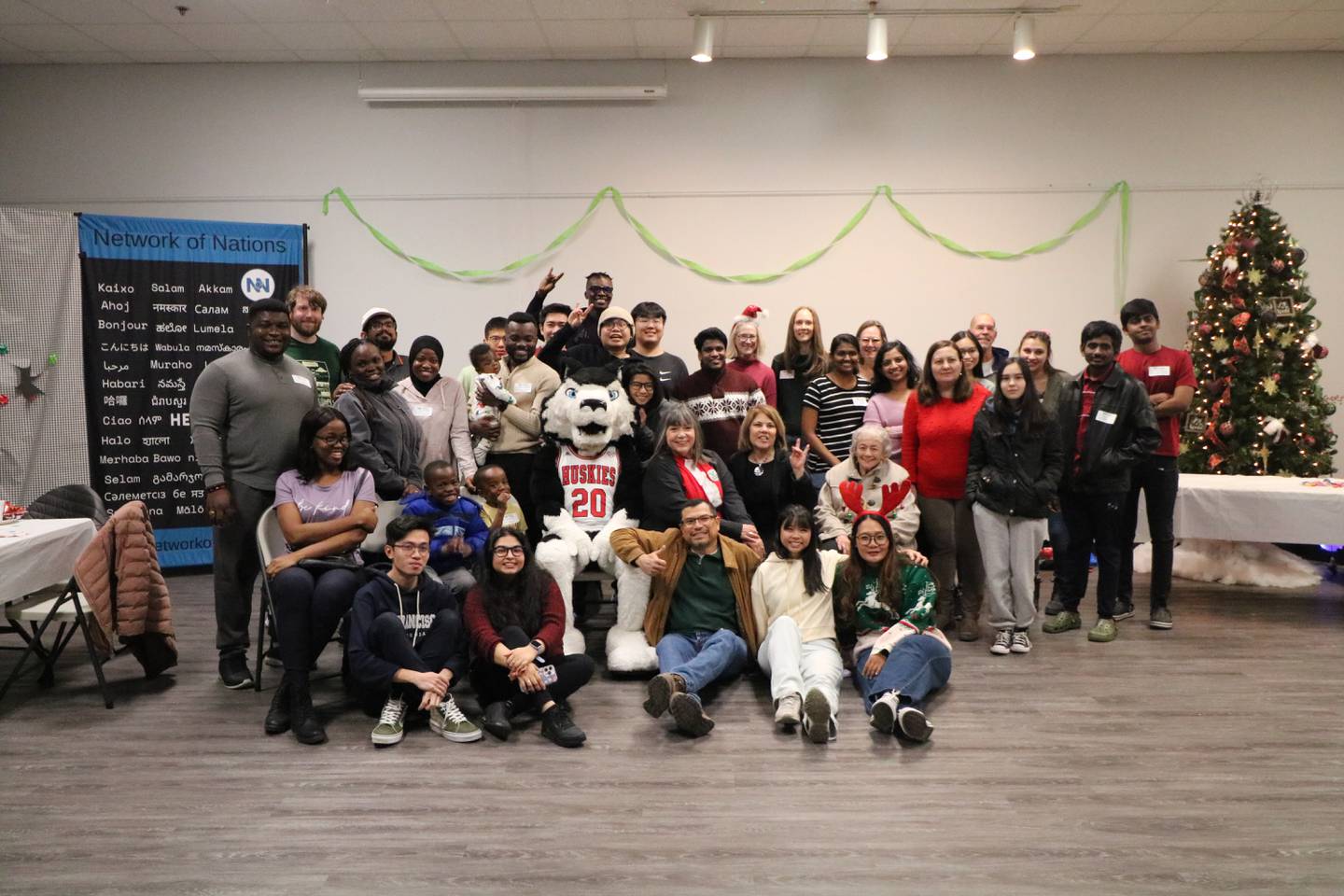 International students and community members pose with NIU's Victor E. Huskie Dec. 13, 2024, during Network of Nation's holiday gathering.