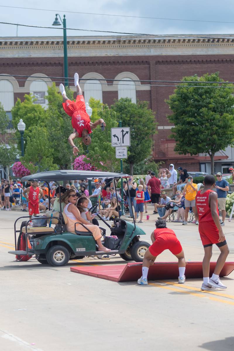 A Jesse White Tumbler flips over a golf cart while taking a video on his phone during the Petunia Festival parade in Dixon on Sunday, July 7, 2024.