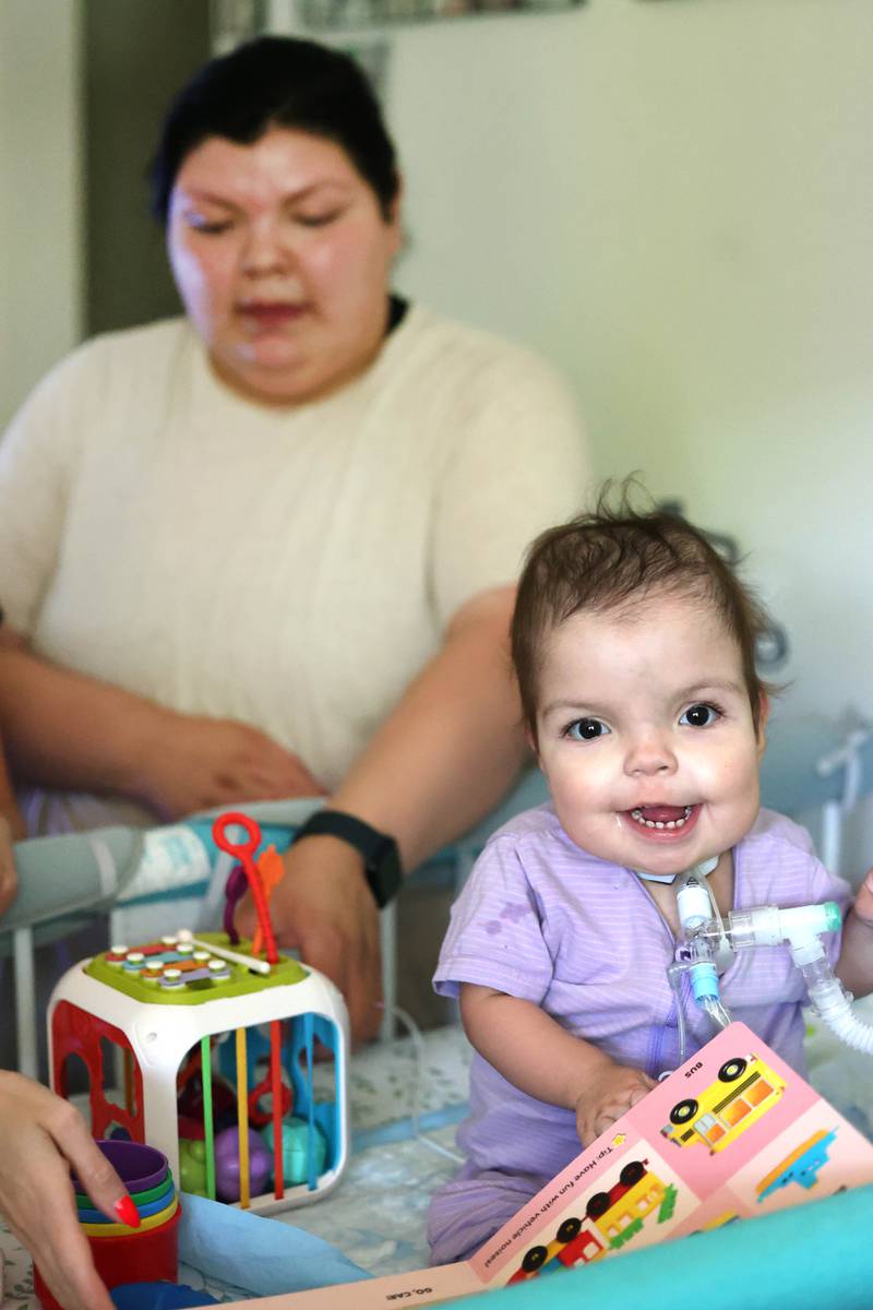 Marely Chavarria Santos, 1, plays in her crib as her mom Kassandra Santos looks on Monday, June 30, 2025, at their home in DeKalb. Marely was born with a myriad of health issues that require around-the-clock care and recently received a heart transplant.