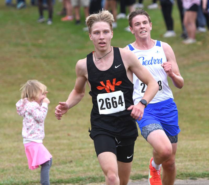 Winnebago's Joseph Erb Jr. (center) sprints to the finish line after avoiding a child on the course at the Amboy Columbus Day Cross Country Invitational held at Shady Oaks Country Club near Amboy on Monday, Oct. 13, 2025. Erb finished ninth.