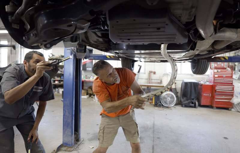 Brad Lundsteen, owner of Suburban Wildlife Control, removes a ball python from a Toyota Crown on Wednesday in Geneva. State Street Collision in Geneva offered the use of a lift to help with the search.