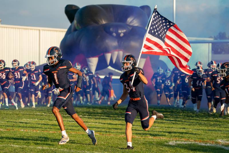 Oswego’s R. Payton Furstenau (34) carries the American flag as Oswego takes the field in their home opener against Neuqua Valley during a football game at Oswego High School on Friday, Aug 26, 2022.