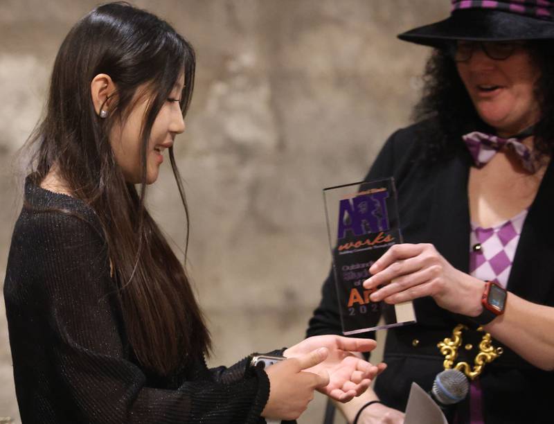 Yijing (Larissa) Zhang, a senior at St. Bede Academy, from China, is handed an award from Mad Hatter Jamie London for her artwork during the 9th annual NCI Artworks Mad Hatter Ball on Friday, Jan. 16, 2026 at the Westclox Event Center in Peru. Zhang, has studied art since she was 4 years old and enjoys photography as well as playing the pipa.