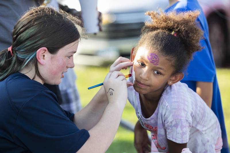 Ayana Pesek, 8, gets a rose face painting by Dixon cheer squad member Alana Lorenzen, 14, Thursday, Aug. 29, 2024, in Dixon. The Dixon PTO hosted their second annual Party in the Playground at Wooden Wonderland as a way to welcome back parents and students and create community within the schools.