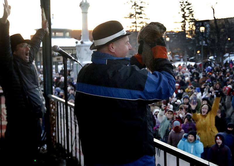 Woodstock Willie is held by handler Mark Szafran as Willie makes his prognostication of six more weeks of winter Thursday, Feb, 2, 2023, while Danny Rubin, the screenwriter of the "Groundhog Day" movie that was filmed in Woodstock, celebrates after announcing Willie’s findings during the annual Groundhog Day Prognostication on the Woodstock Square.