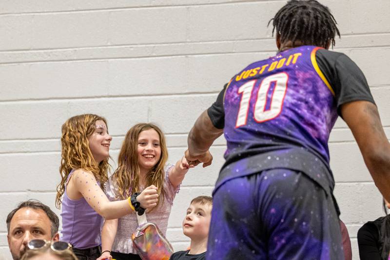 Deven “Just Do It” Dorsett (10) of the Harlem Wizards fist-bumps (left to right) Tessa Galyen and Gwen Wissea on Wednesday, April 16, 2025 at Woodland High School in Streator.