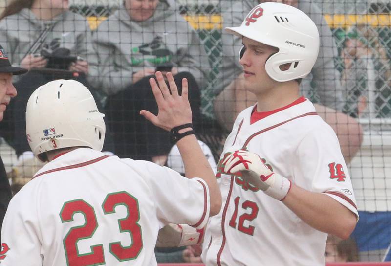 L-P's Brendan Boudreau hi-fives teammate Brady Backes after scoring a run against Alleman on Tuesday, March 12, 2024 at the L-P Athletic Complex in La Salle.