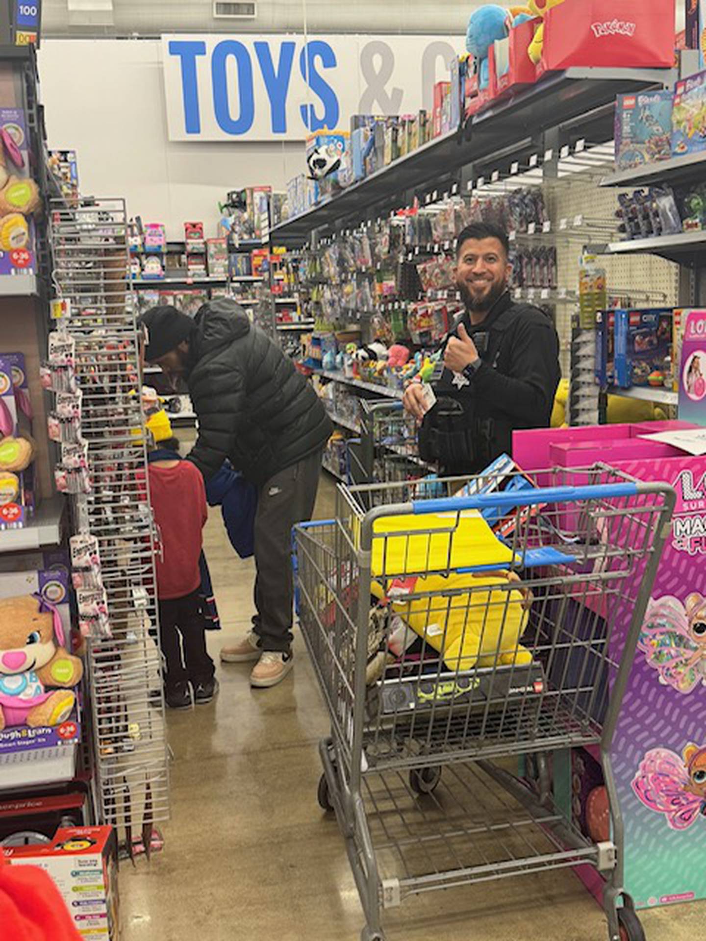 Officer Lopez is on stand-by as a kid fills the shopping cart with toys during Plano Police Department's Shop with a Cop event.