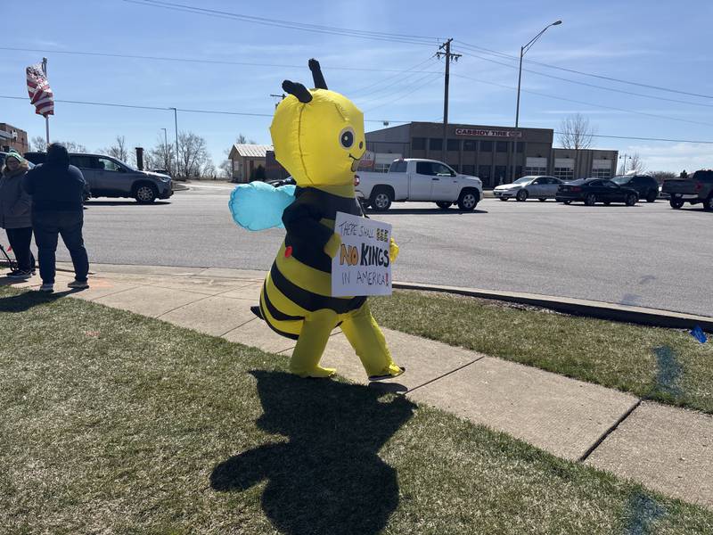 An attendee in a bee costume holds a sign  at a No Kings rally in Crystal Lake, Saturday, March 28, 2026.
