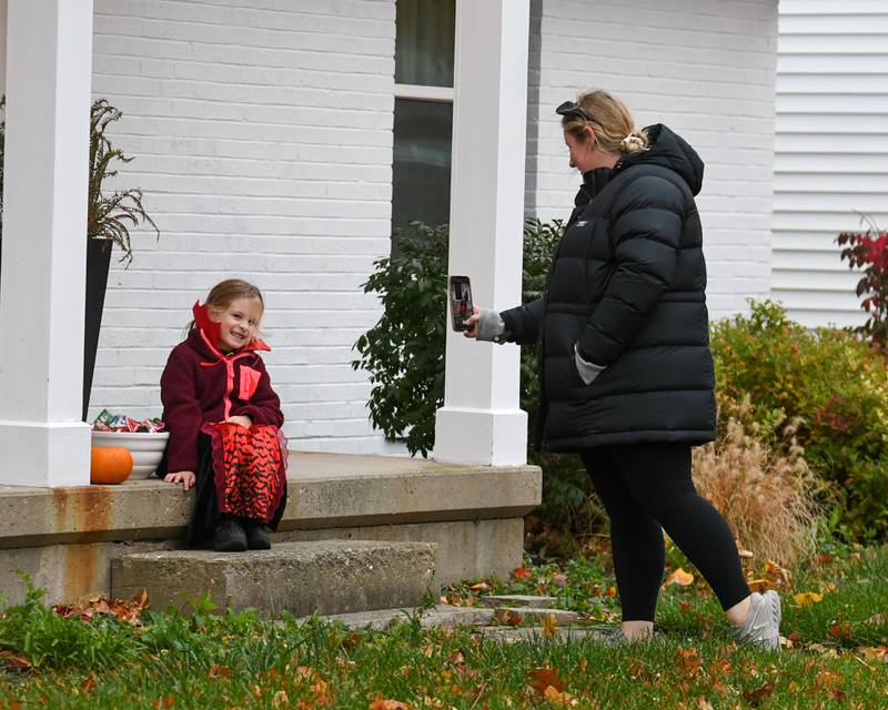 Katie Blum, mom, takes a picture of her daughter Emma Cann, 5, as Emma waits for trick-or-treaters to hand out Halloween candy on Thursday, Oct. 31, 2024, in DeKalb.