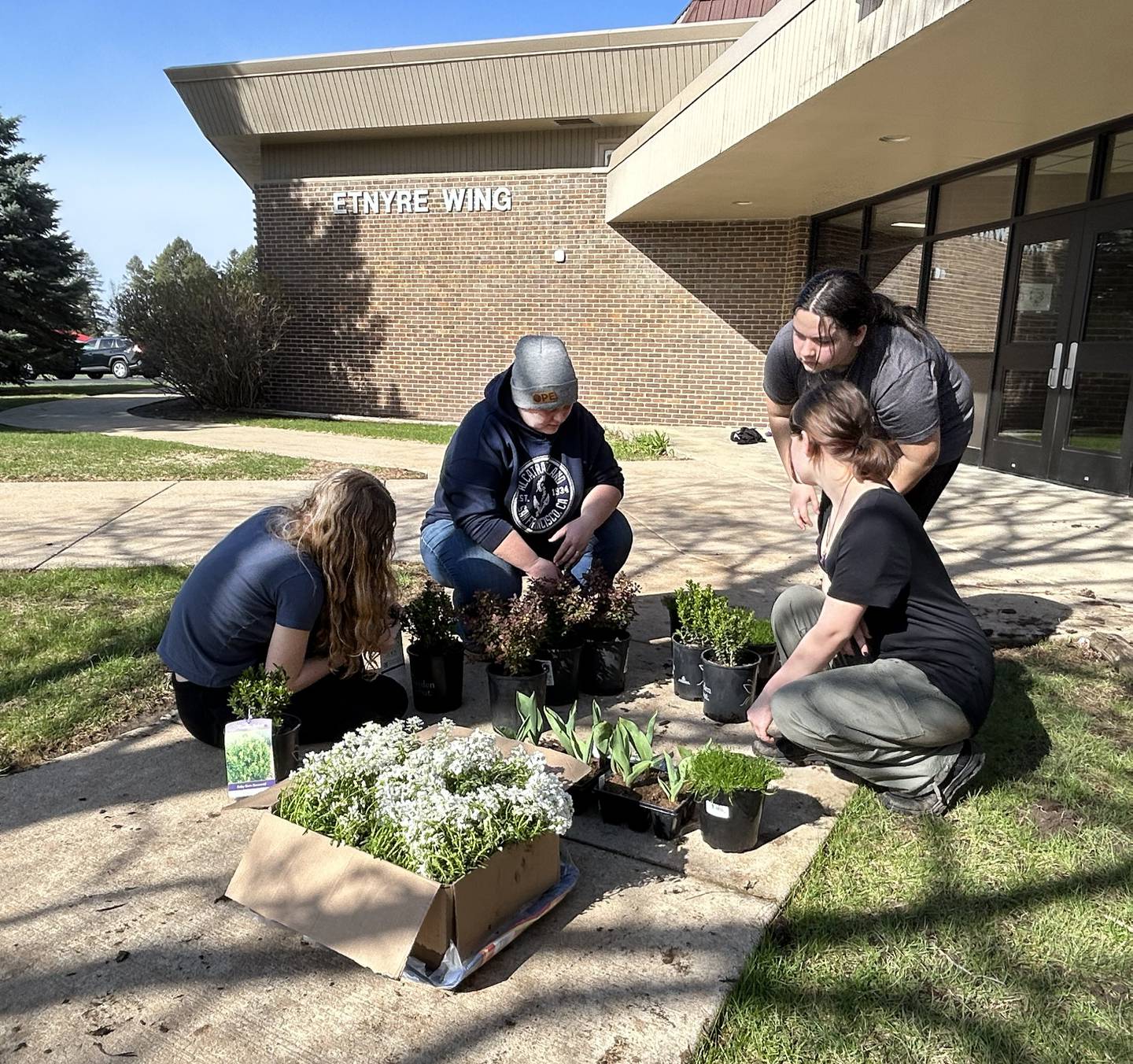 Oregon School District staff member, Lindsey Breeden (center) directs students as they spruce up landscaping near the Etnyre wing's gym entrance on Saturday, April 5, 2025.