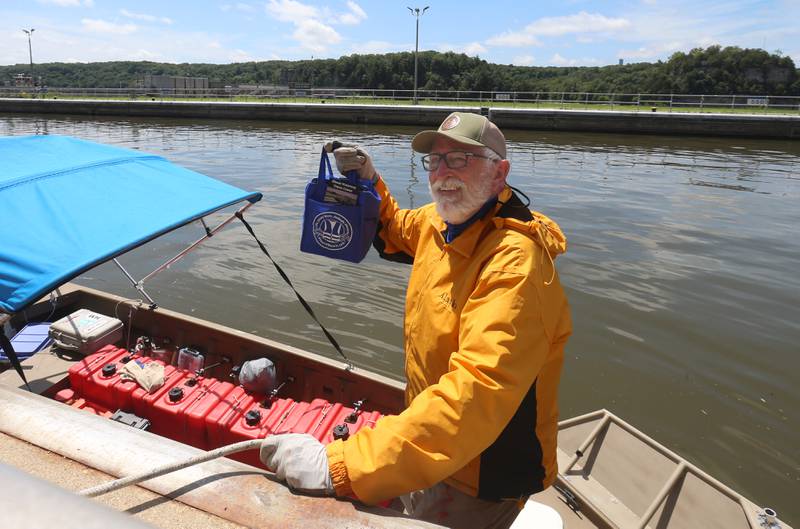 71 year old adventurer and thyroid cancer survivor Robert Youens, holds a bag of goodies from the Illinois Waterway Visitors Center while locking at the Starved Rock Lock and Dam on Monday, July 28, 2025 near Utica. Youens is making  the Great Loop, a 6,000 mile journey on his Jon boat something that hasn't been done before. Youens is looking at setting a record for the longest someone has gone on a Jon boat.