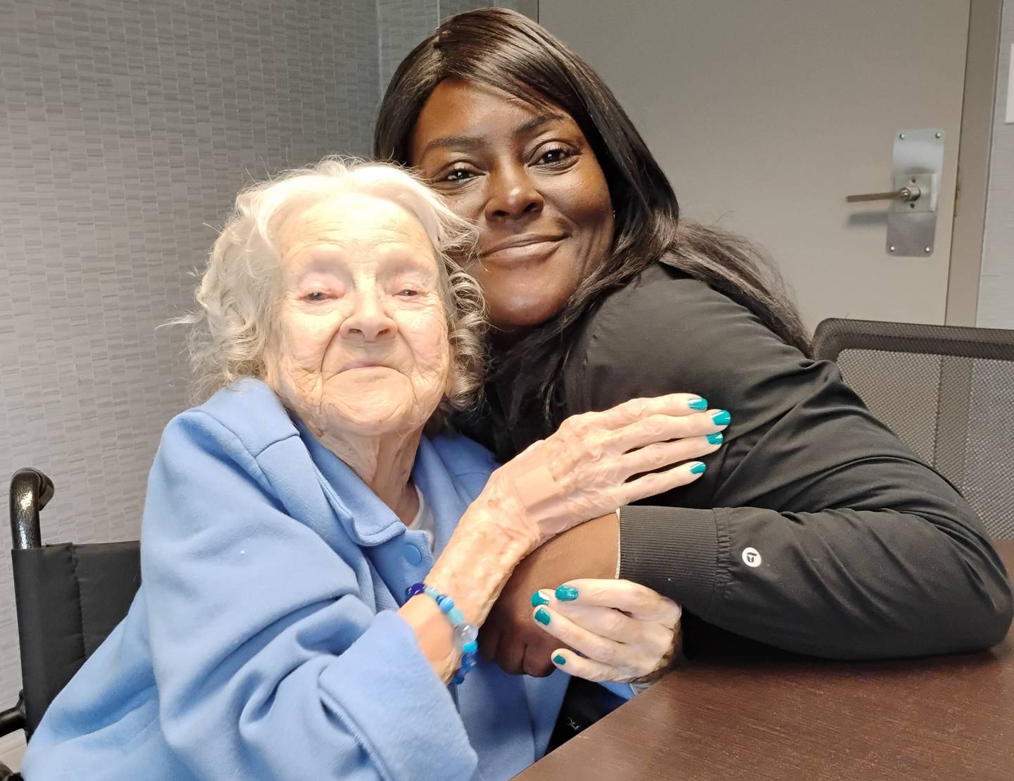 Helen Frank gets a hug from Crescent Care Activity Director Shamell Dew during an interview with a reporter. Because Frank – at 104 and counting – didn't wear her hearing aids, Dew repeated each question directly into her good ear. Frank  celebrated being 105 at a party Tuesday, May 12, 2026, at Crescent Care in Elgin.