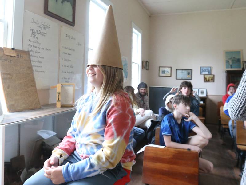 Josh May, a student with the Bureau County Special Schools BEST Program, wears a dunce cap during a field trip to Aitken School on Tuesday, May 20, 2025 at the La Salle County Historical Society in Utica. Aitken School is a one-room schoolhouse located on the campus of the La Salle County Historical Society. If a child was being disrespectful in the 1800s, they would extend their arms out and hold books in their hand.