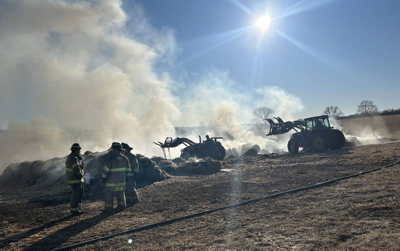 Firefighters from several departments responded to a field and hay bale fire at a farm on West Pines Road between Polo and Oregon on Monday, Feb. 23, 2026. Here, farmers use tractors to carry and separate the burning bales in an open area where firefighters could extinguish them.