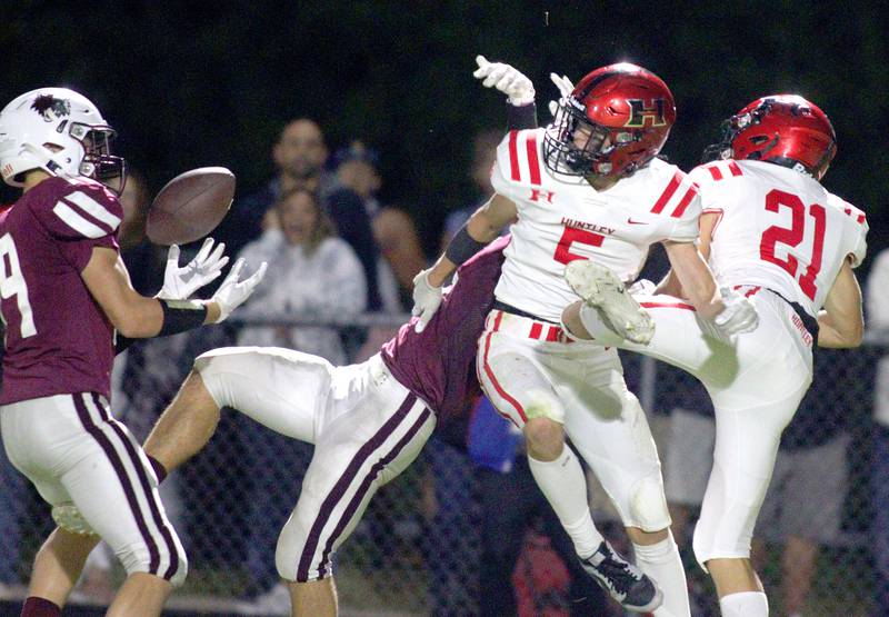 Huntley’s Zach Rysavy, center, watches as Prairie Ridge’s Michael Dimarco, left, snags a deflected ball on a pass play in varsity football at Crystal Lake Friday night.