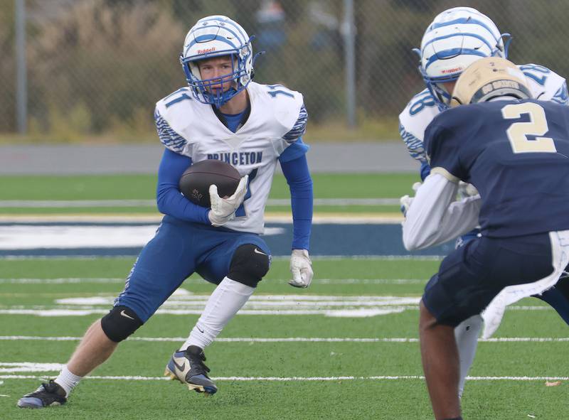 Princeton's Braden Shaw runs with the ball as teamamte Ayden Agushi blocks Central Catholic's Keshaun Manney from getting to the play during the Class 3A playoffs on Saturday, Nov. 1, 2025 at Central Catholic High School in Bloomington.