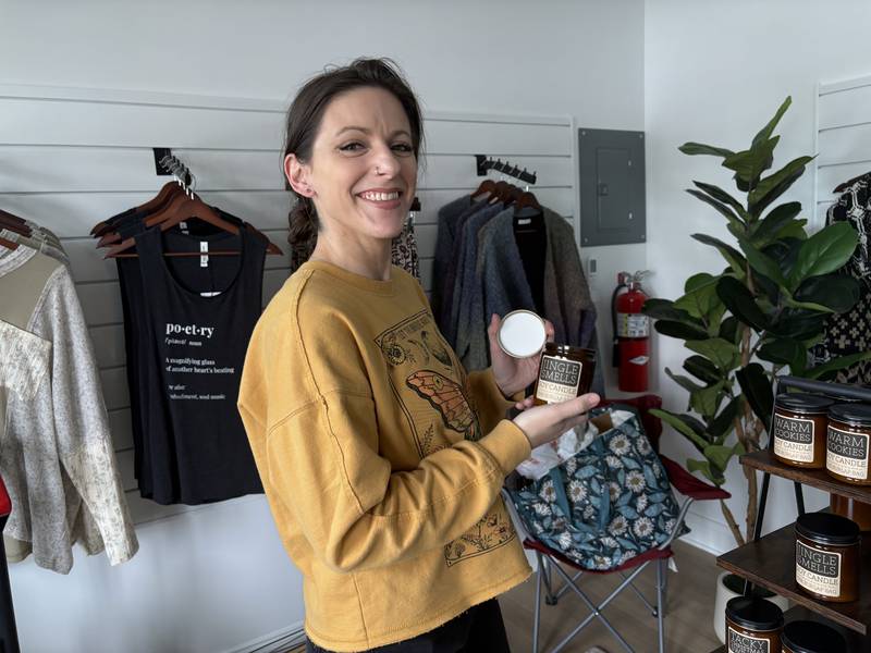 Denae Hintze shows off a candle at her Huntley store, Wild in Ink, Oct. 28, 2025.