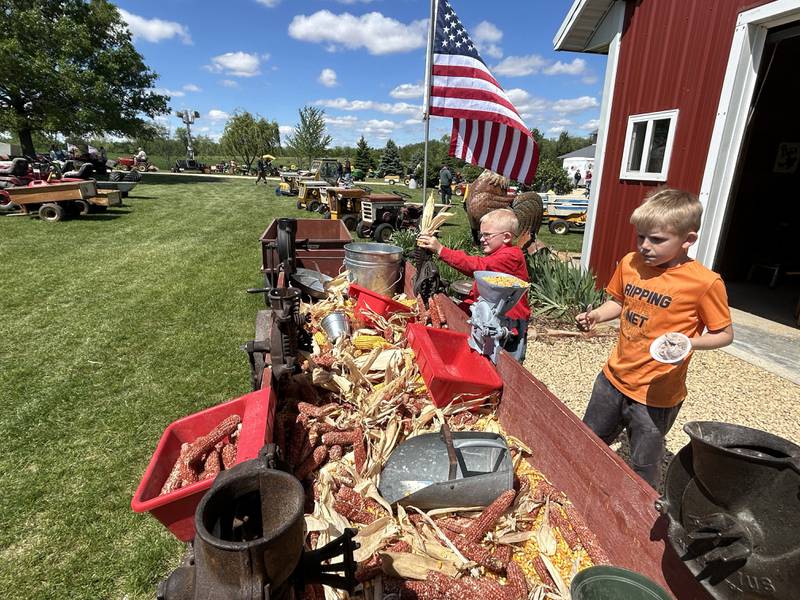 Easton James, 7, of Oregon, (center) runs a hand sheller as Kyler Kitson, 8, of Harvard, eats ice cream as he "supervises" during the 16th Annual AJ’s Garden Tractor Jamboree on Saturday, May 17, 2025.