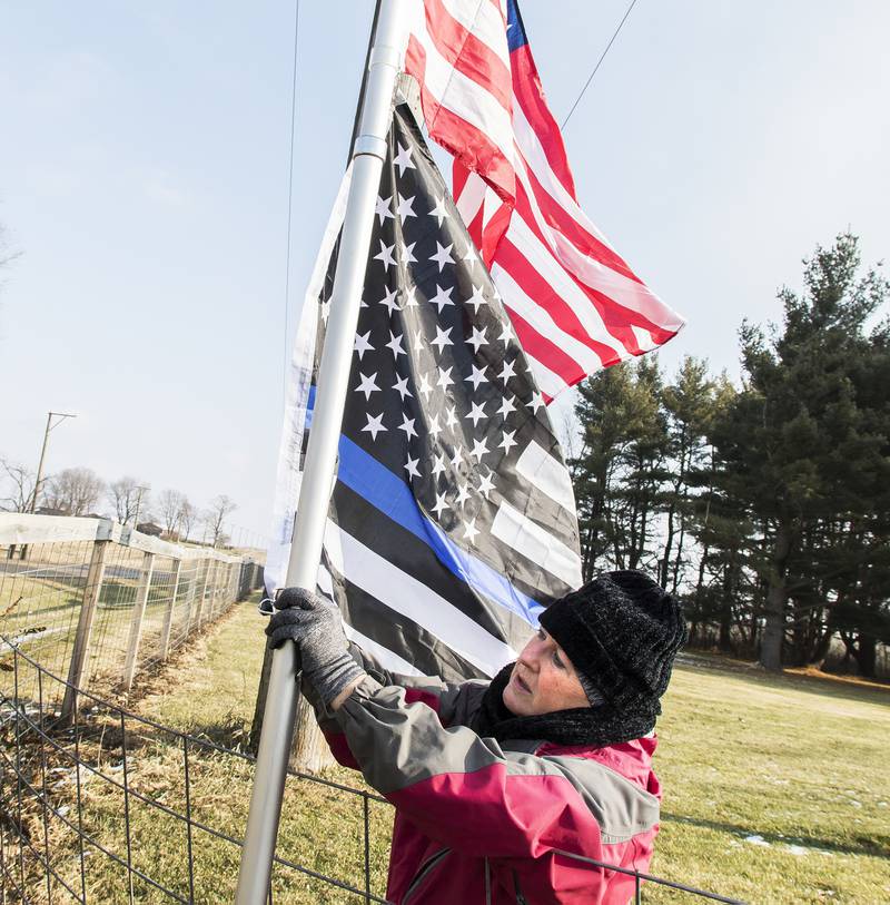 Karen Davis raises an American flag and a thin blue line flag on her property along Flagg Road in in 2020 as a tribute to fallen police officers. This year, Davis is planning a tribute to fallen firefighters and will light a glow stick in honor of each fallen officer in 2021.