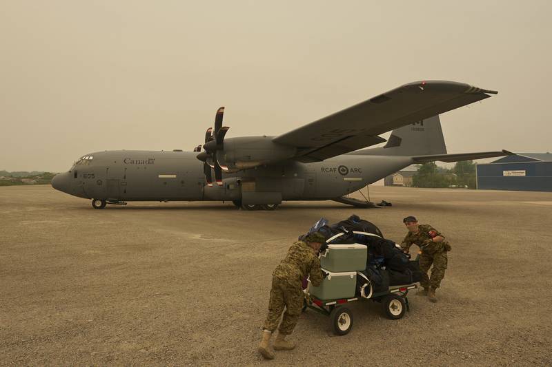 Royal Canadian Air Force Pte. Carter Brinn (left) and Cpl. Ethan Cai helps load cargo as evacuees from Pinaow Wachi Care Home board a C-130 Hercules aircraft in Norway House, Man., Tuesday, June 3, 2025, at the Norway House Airport as crews continue to fight wildfires in northern Manitoba. (David Lipnowski/The Canadian Press via AP)