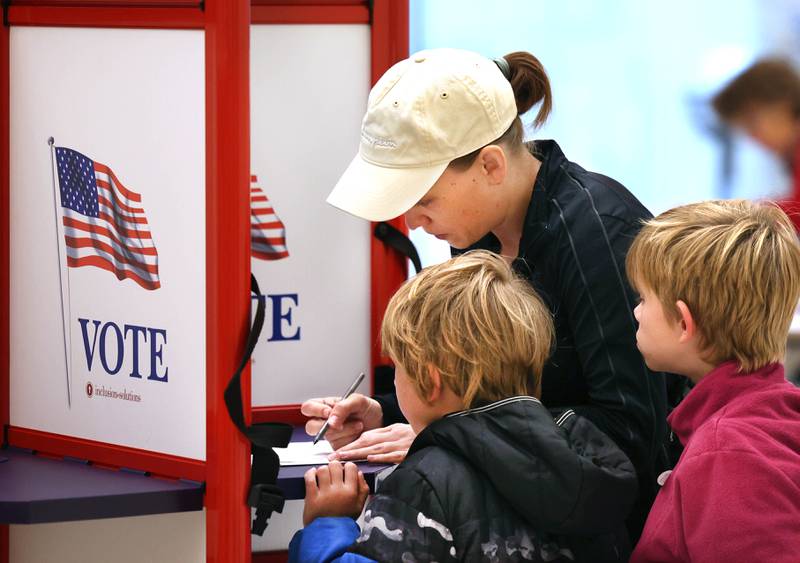 Kay Aldrich, from DeKalb, shows her kids Oliver Eich, (left) 6, and Elliott Eich, 7, the voting process Tuesday, Nov. 5, 2024, as she casts her ballot on Election Day at the DeKalb Public Library.