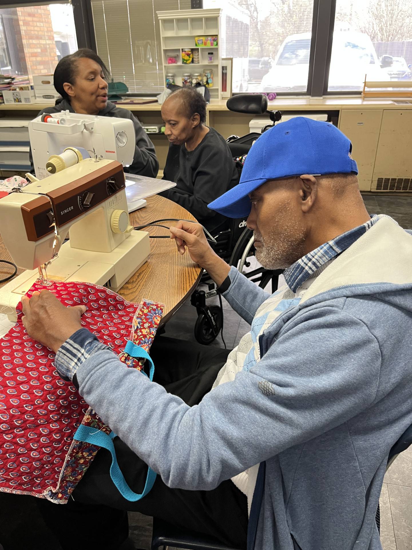 Melvin Booker (front) focused on sewing his tote bag as Cassandra Farley, director of adult services, (left) helped Lula Green (right) get ready to take the next step on hers.
