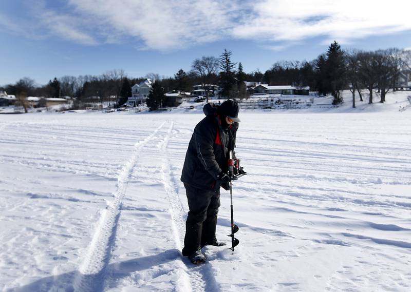 Trevor Janes, who owns Wet N Wild Outfitters, drills a hole in the ice while ice fishing Friday, Feb 3. 2023, on Petite Lake near Fox Lake.