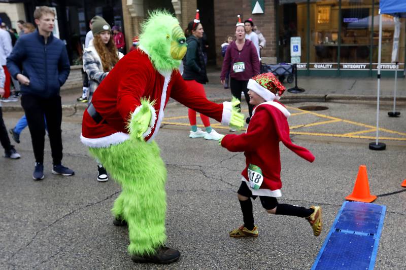 Russ Hyatt of Sundowner Entertainment, dressed as the Grinch greats 
Aaden Barcus as he finishes the 5K race in the McHenry County Santa Run For Kids on Sunday morning, Dec. 3, 2023, in Downtown Crystal Lake. The annual event raises money for agencies in our county who work with children in need.