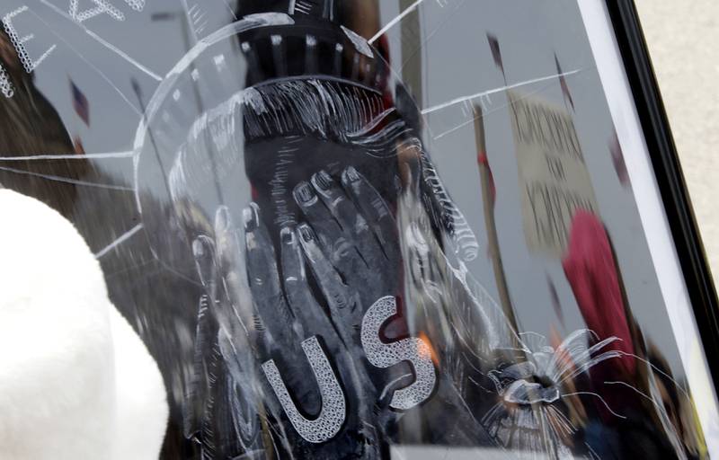 Protesters are reflected in picture carried by a protester of Lady Liberty lon Saturday, March 28, 2026, during the McHenry County No Kings Protest. According to an organizer, over 4,000, people took part in the protest.